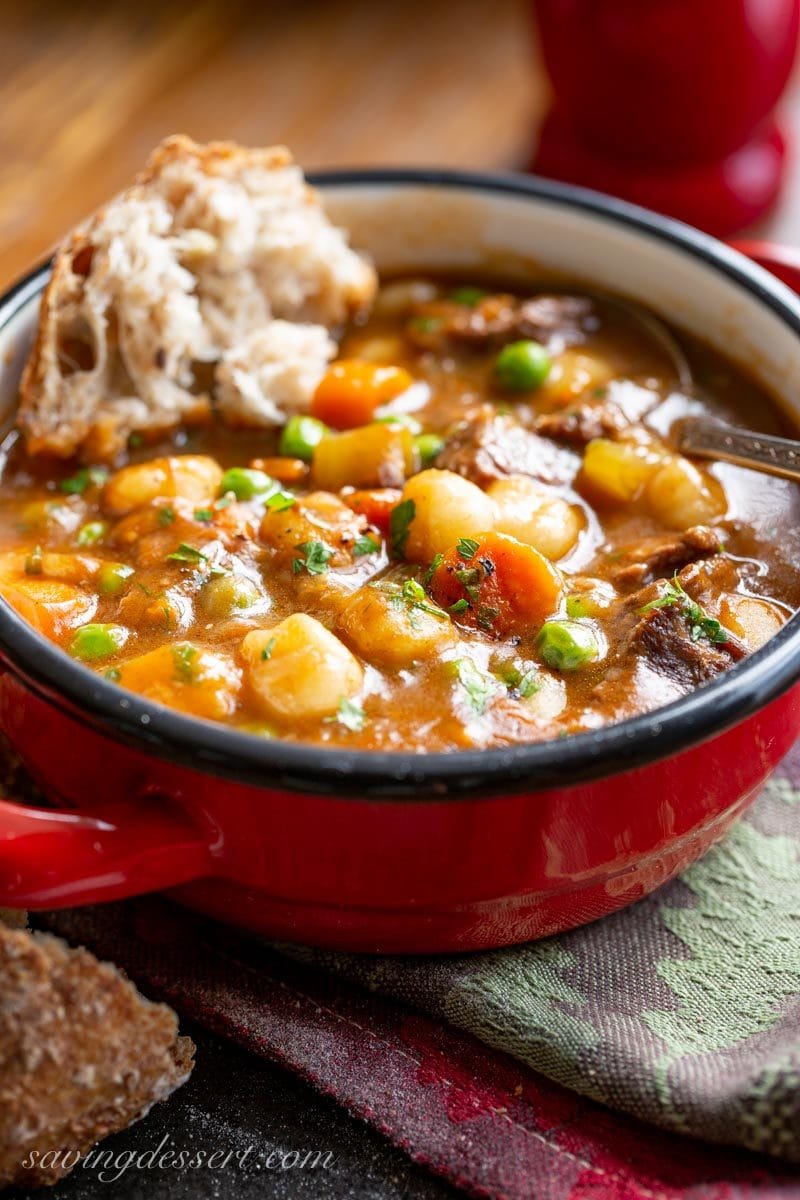 A bowl of hearty beef and gnocchi soup with vegetables and crusty bread