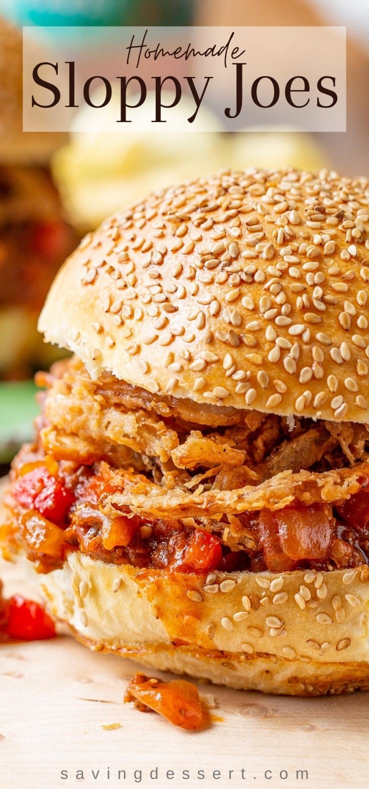 A close up of a sloppy joe sandwich topped with crispy onions on a toasted sesame seed bun