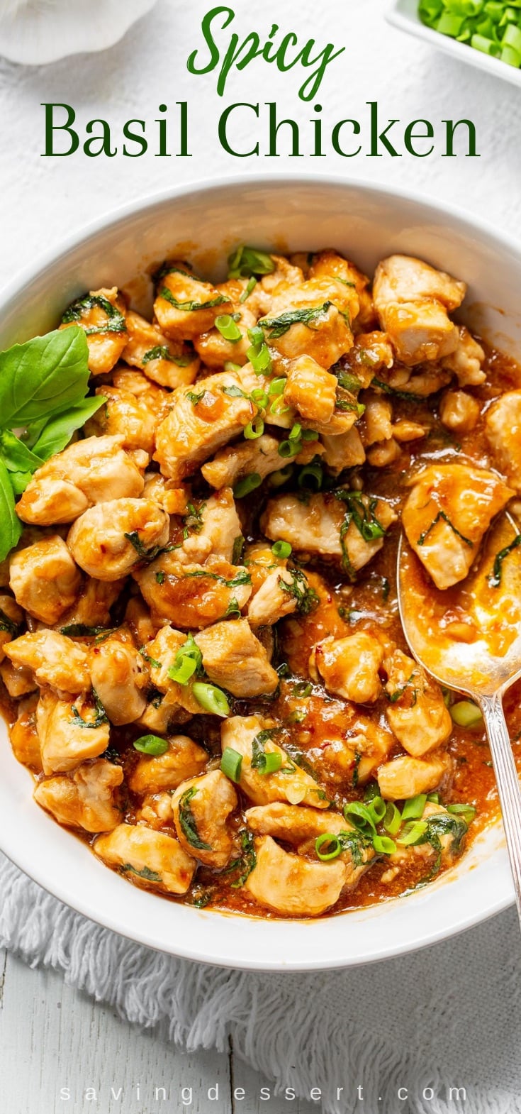 A bowl of spicy basil chicken garnished with sliced green onions