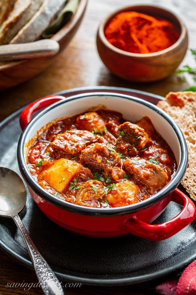 A bowl of Hungarian style Beef Goulash with potatoes and plenty of red sweet paprika. Served with bread and topped with fresh chopped parsley