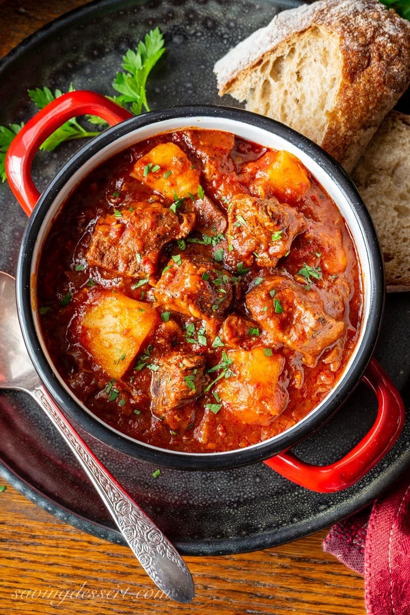 A bowl of Hungarian style Beef Goulash served with bread and topped with chopped fresh parsley leaves