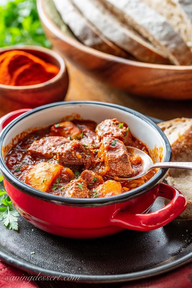 a spoonful of tender beef from a bowl of Hungarian style beef Goulash. Served with bread and topped with fresh chopped parsley