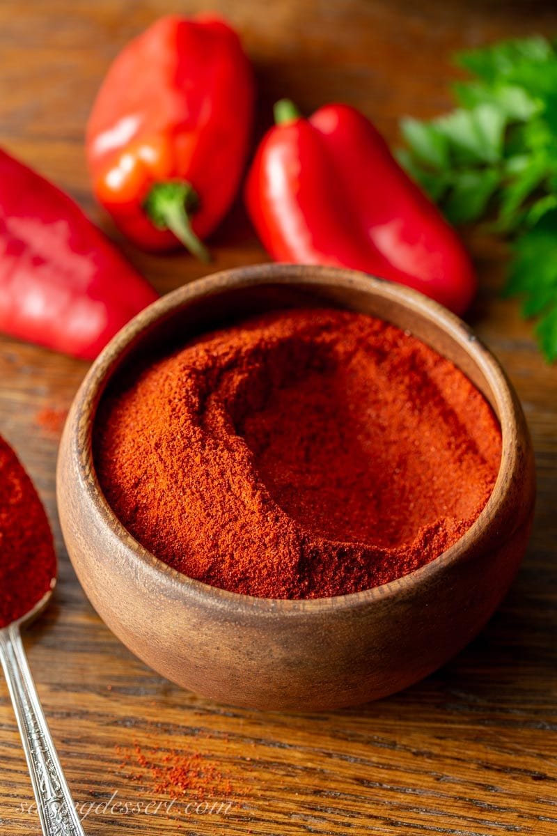 A wooden bowl of sweet Hungary paprika with red peppers and fresh parsley