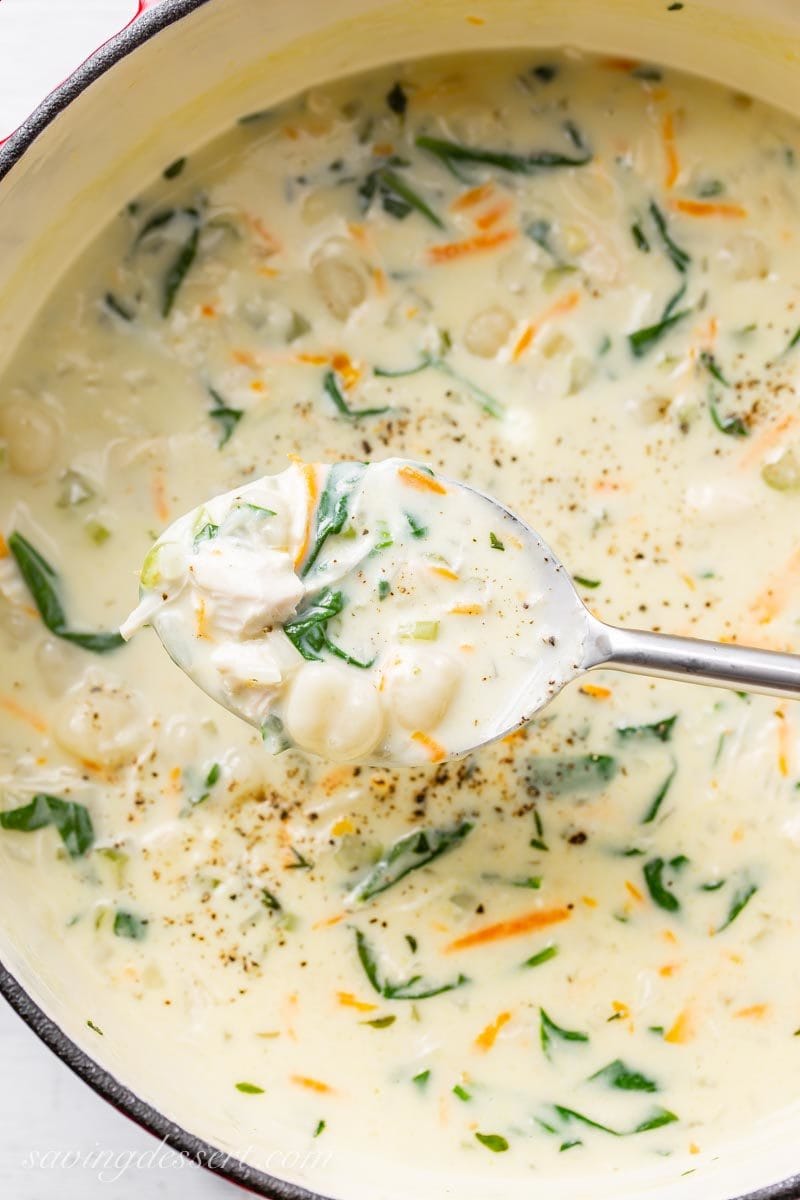 A pot of creamy chicken gnocchi soup with shredded carrots, spinach and plenty of fresh ground black pepper