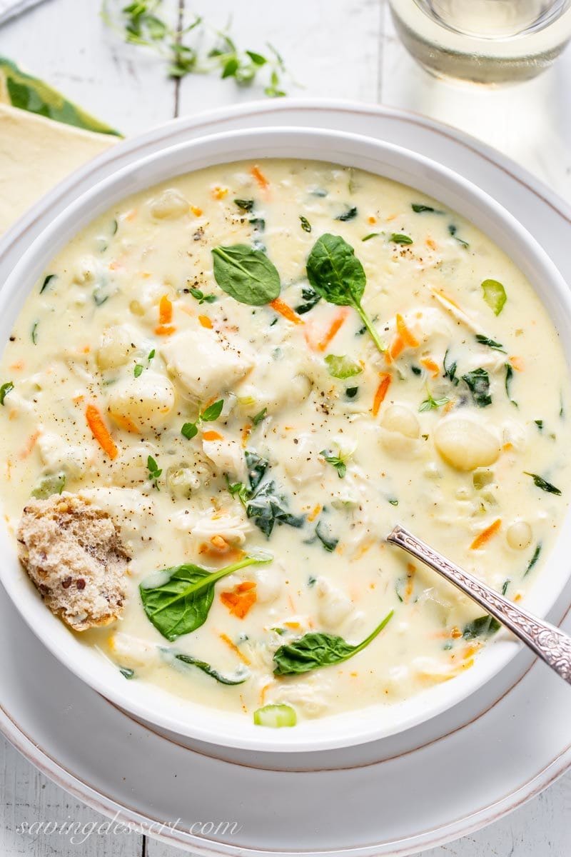 A bowl of creamy chicken gnocchi soup with spinach, shredded carrots and a piece of crusty bread