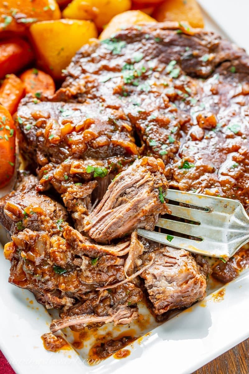 A platter with carrots potatoes and a fork tender oven braised pot roast