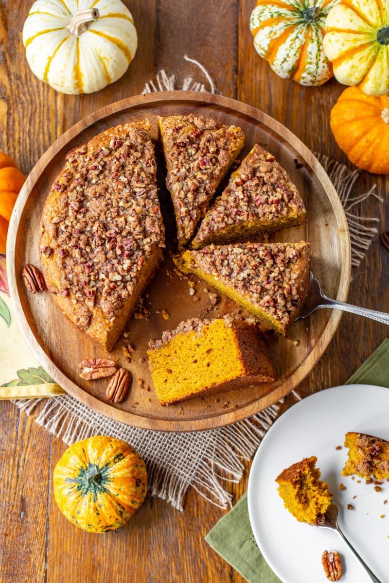 An overhead view of a sliced Pumpkin Breakfast Cake with pecan crumble topping on a cake plate