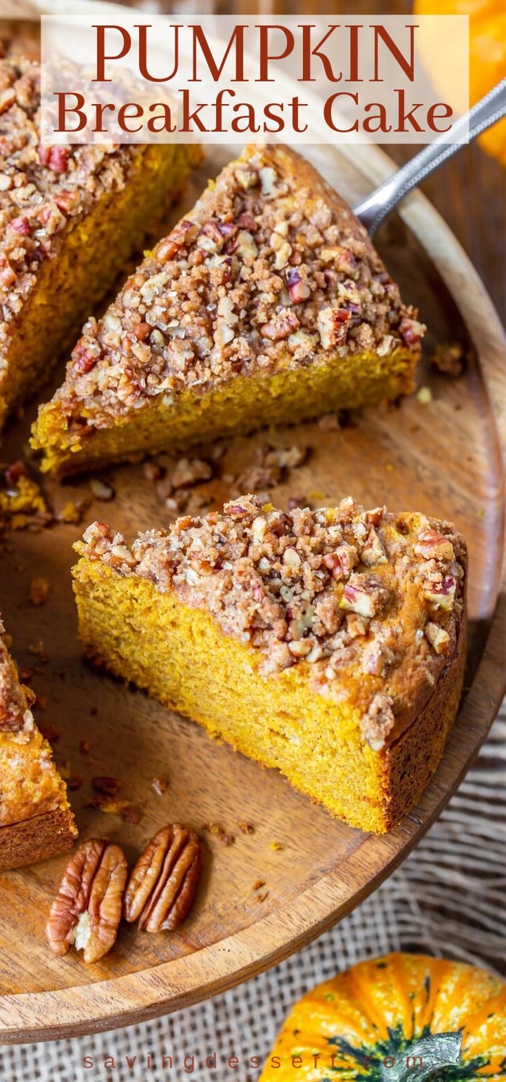 A sliced pumpkin breakfast cake on wooden cake plate with a pecan crumble topping