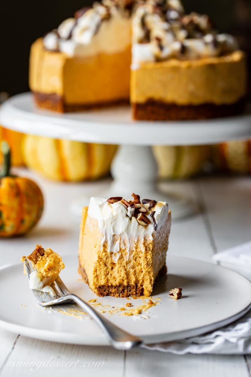 A slice of no bake pumpkin cheesecake on a gingersnap crust topped with whipped cream cheese topping, caramel and chocolate drizzles and toasted pecans.
