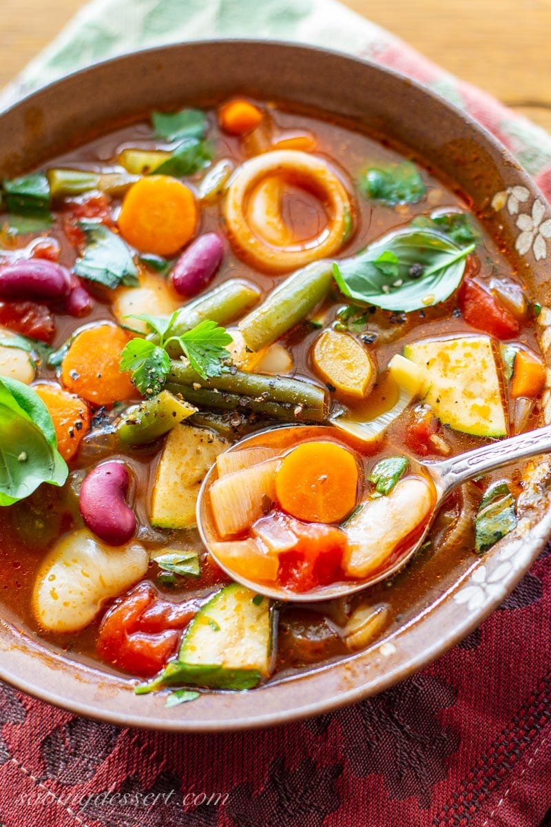 A bowl of chunky vegetable soup with beans, tomatoes, fresh basil leaves, green beans and leeks.