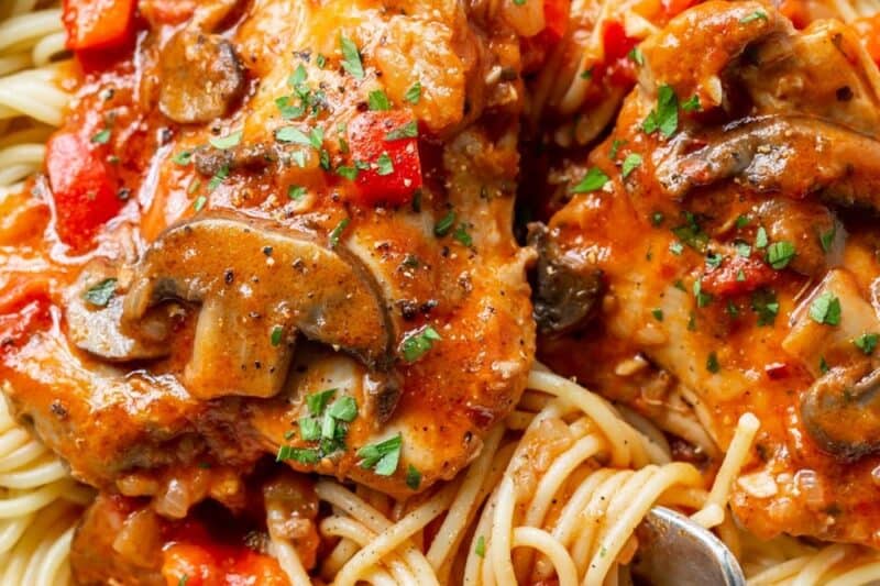 An overhead view of a bowl of spaghetti topped with saucy chicken cacciatore.