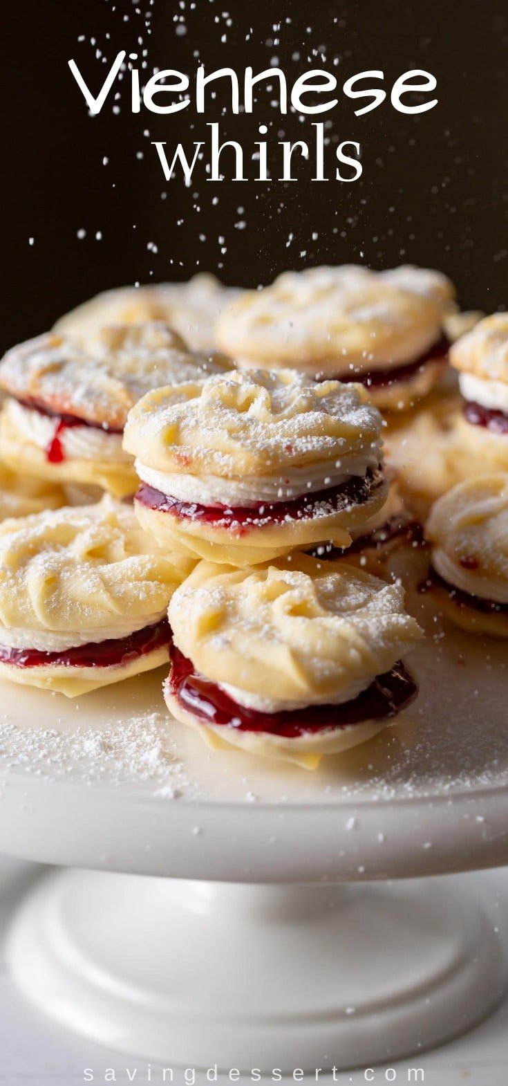 A cake platter stacked with butter cookies sandwiched with raspberry jam and buttercream frosting