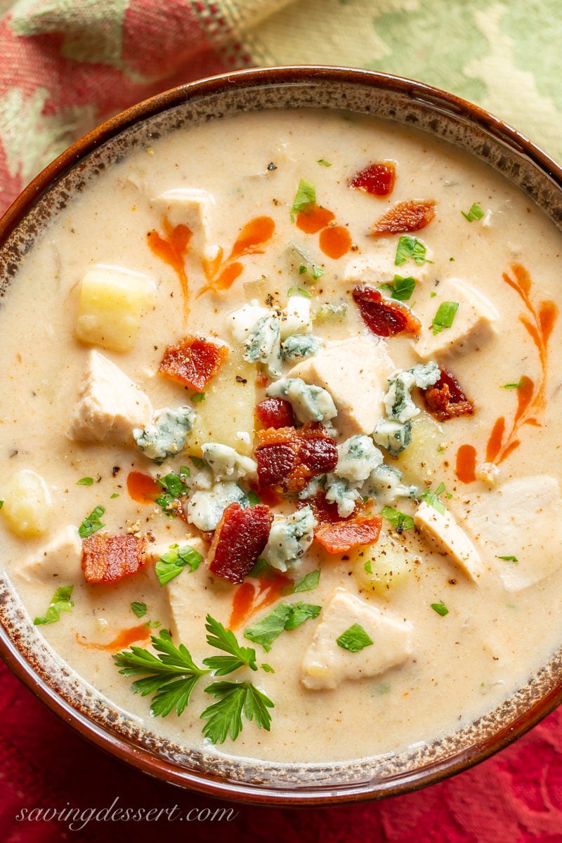 A bowl of buffalo chicken soup garnished with hot sauce, bacon and parsley