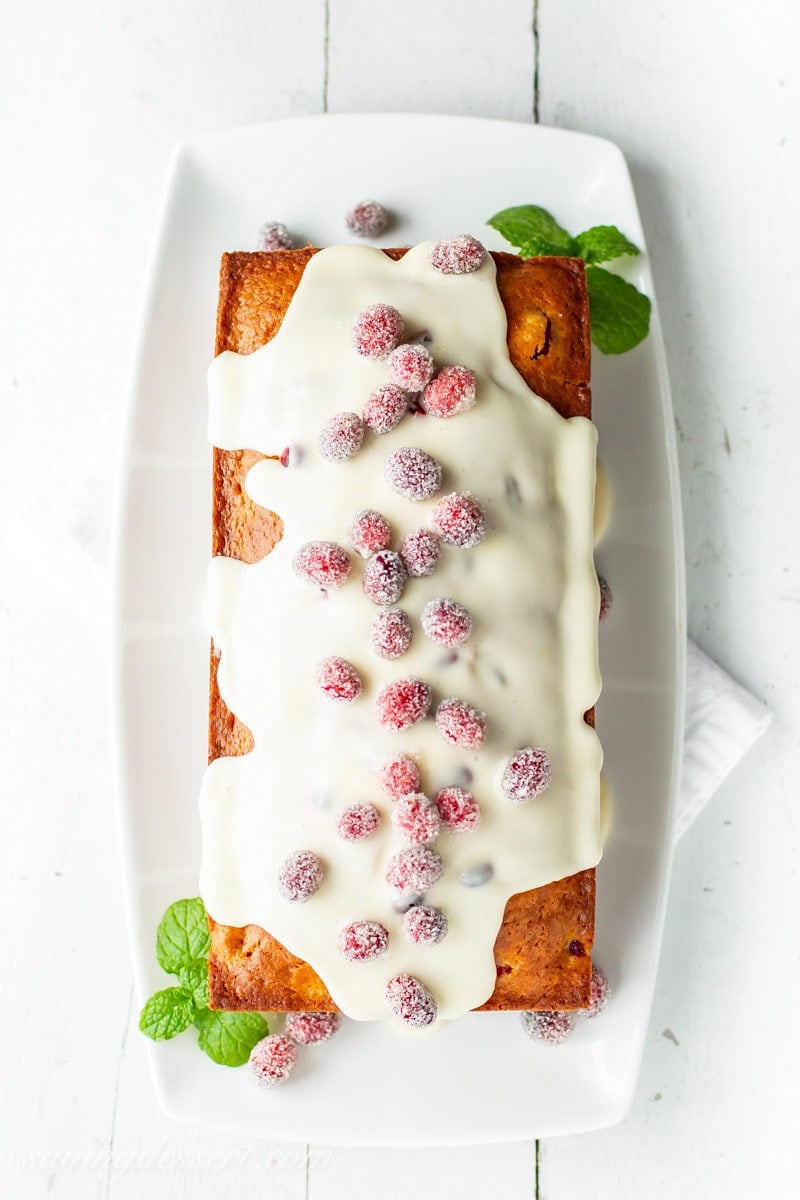 An overhead view of a loaf of Cranberry Orange Bread with orange icing and sugared cranberries on top