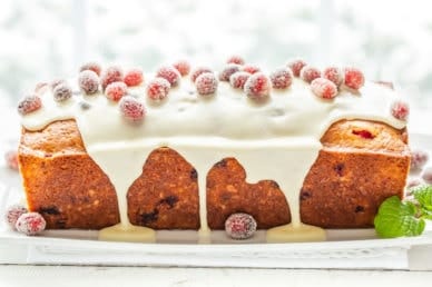 A side view of a loaf of cranberry orange bread topped with a dripping icing and sugared cranberries