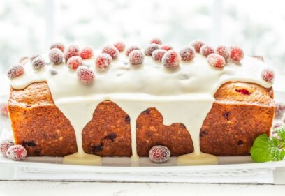 A side view of a loaf of cranberry orange bread topped with a dripping icing and sugared cranberries