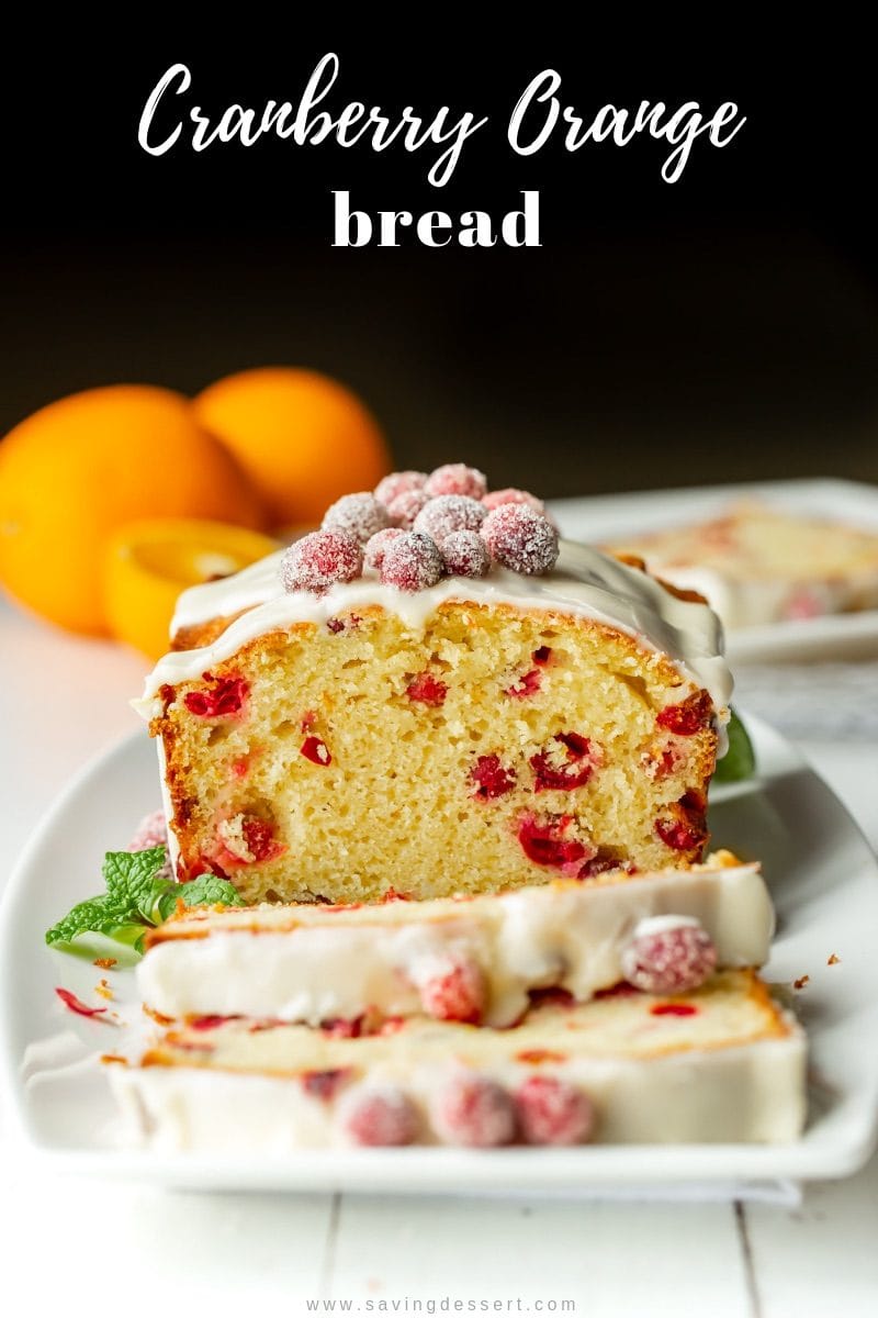 A sliced Cranberry Orange Bread with an orange glaze icing and sugared cranberries on top