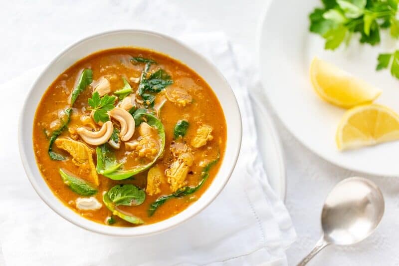 A bowl of creamy coconut chicken soup with spinach, lentils and cashews