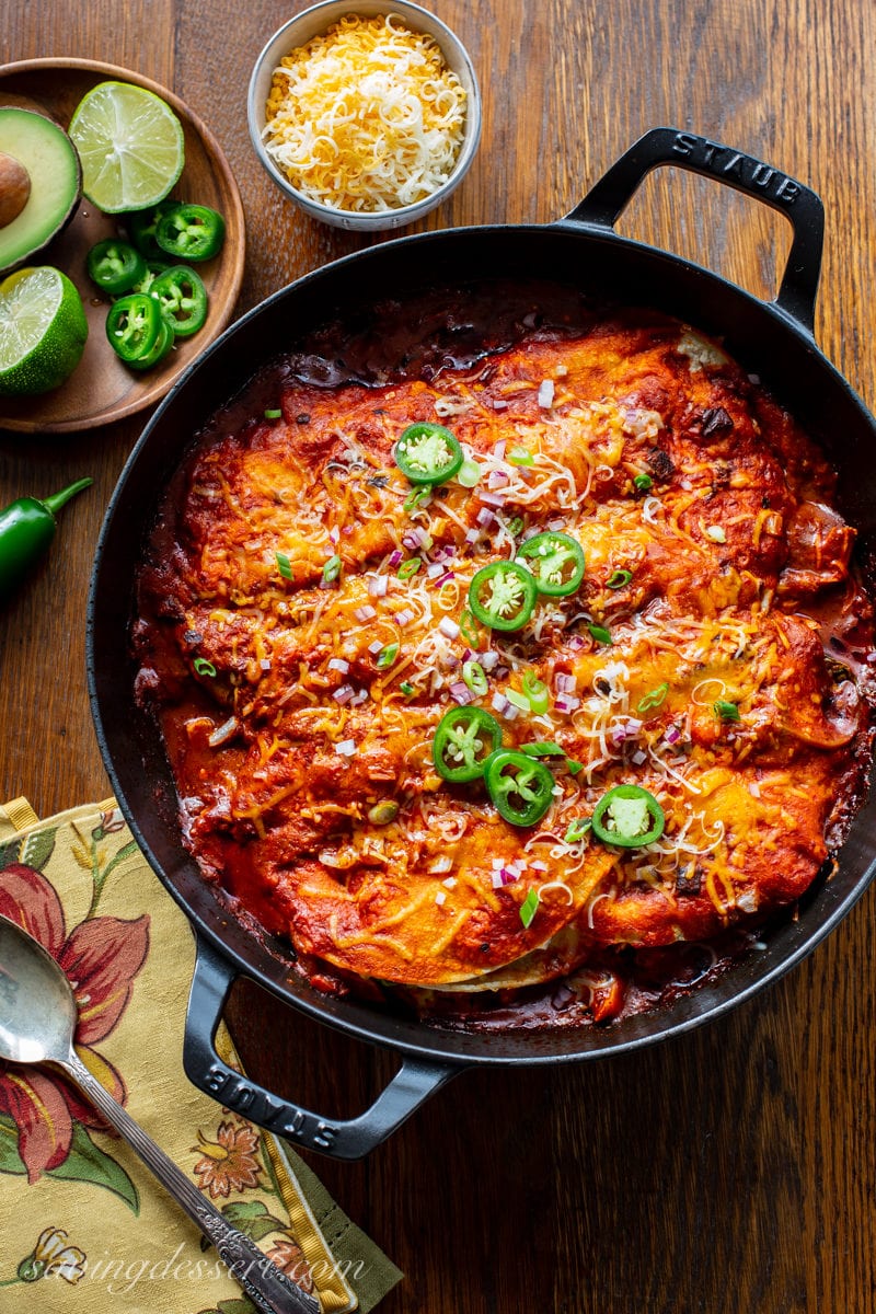 A skillet with chicken enchiladas topped with sliced jalapeño peppers, onions and cheese.