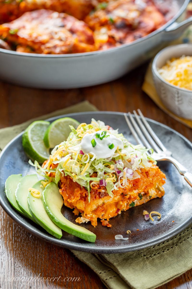 A plate of chicken enchiladas with avocado, lime, shredded lettuce and sour cream