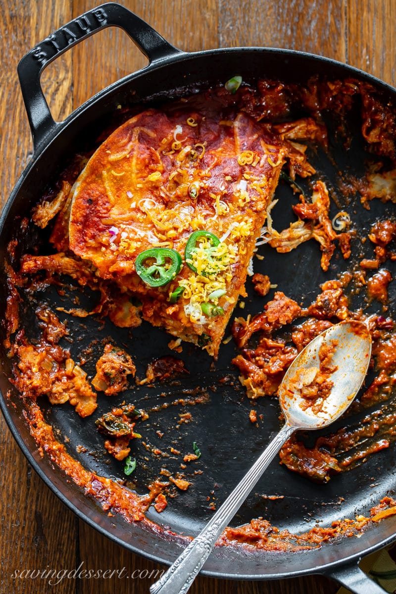 An almost empty skillet of chicken enchiladas with a spoon