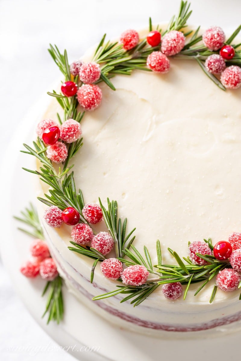 An overhead shot of red velvet cake decorated with rosemary and sugared cranberries