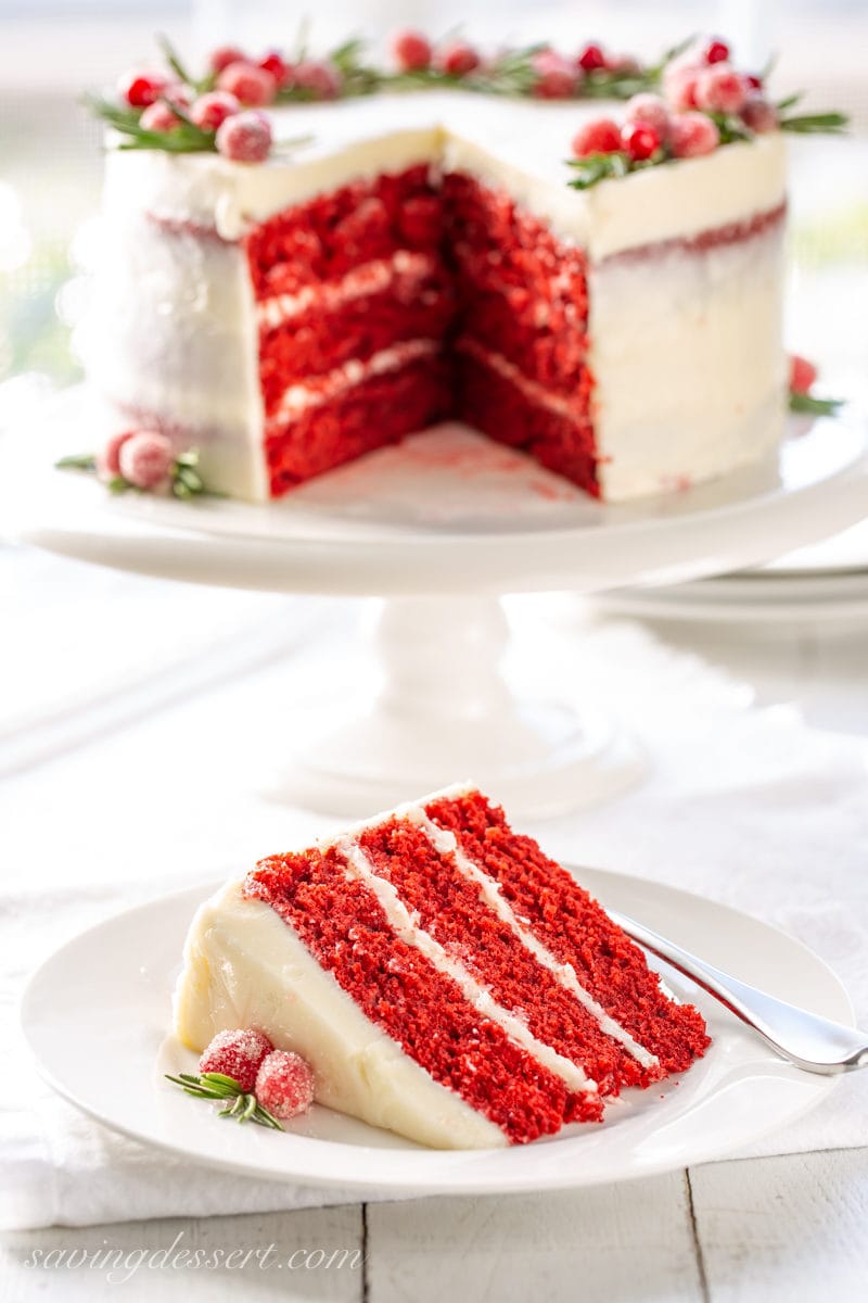 A slice of red velvet cake with sugared cranberries and rosemary sprigs forming a festive wreath on top