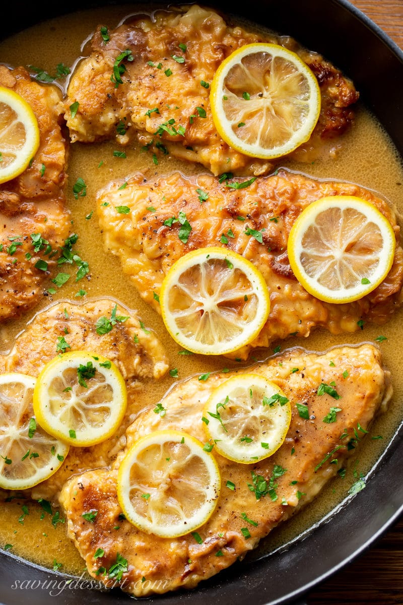 Chicken Francese - a skillet with tender, breaded chicken cutlets in a simple buttery, lemon sauce. Garnished with sliced lemons and fresh chopped parsley