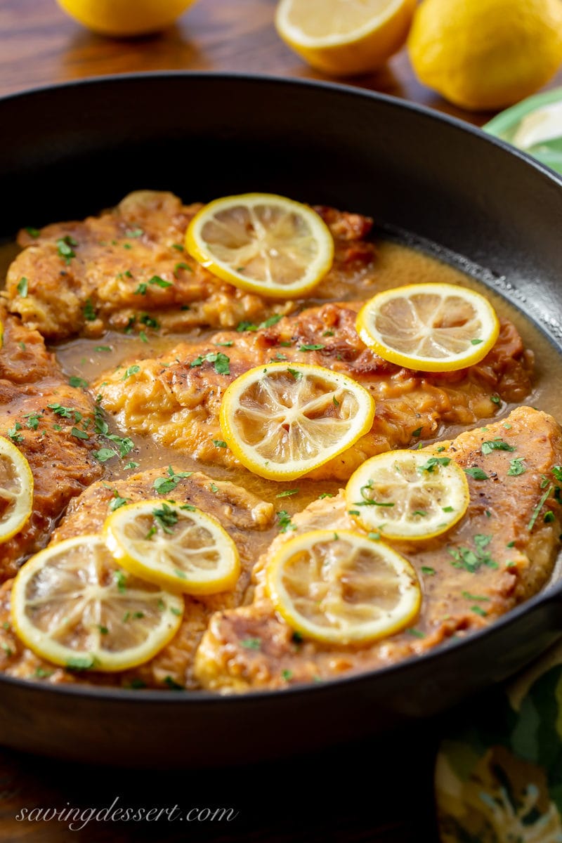 Askillet with tender, breaded chicken cutlets in a simple buttery, lemon sauce. Garnished with sliced lemons and fresh chopped parsley