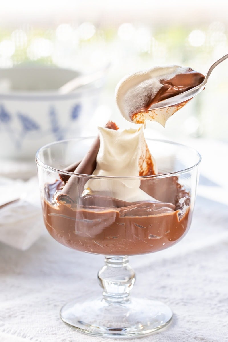 A cup of homemade chocolate pudding with whipped cream and a chocolate curl