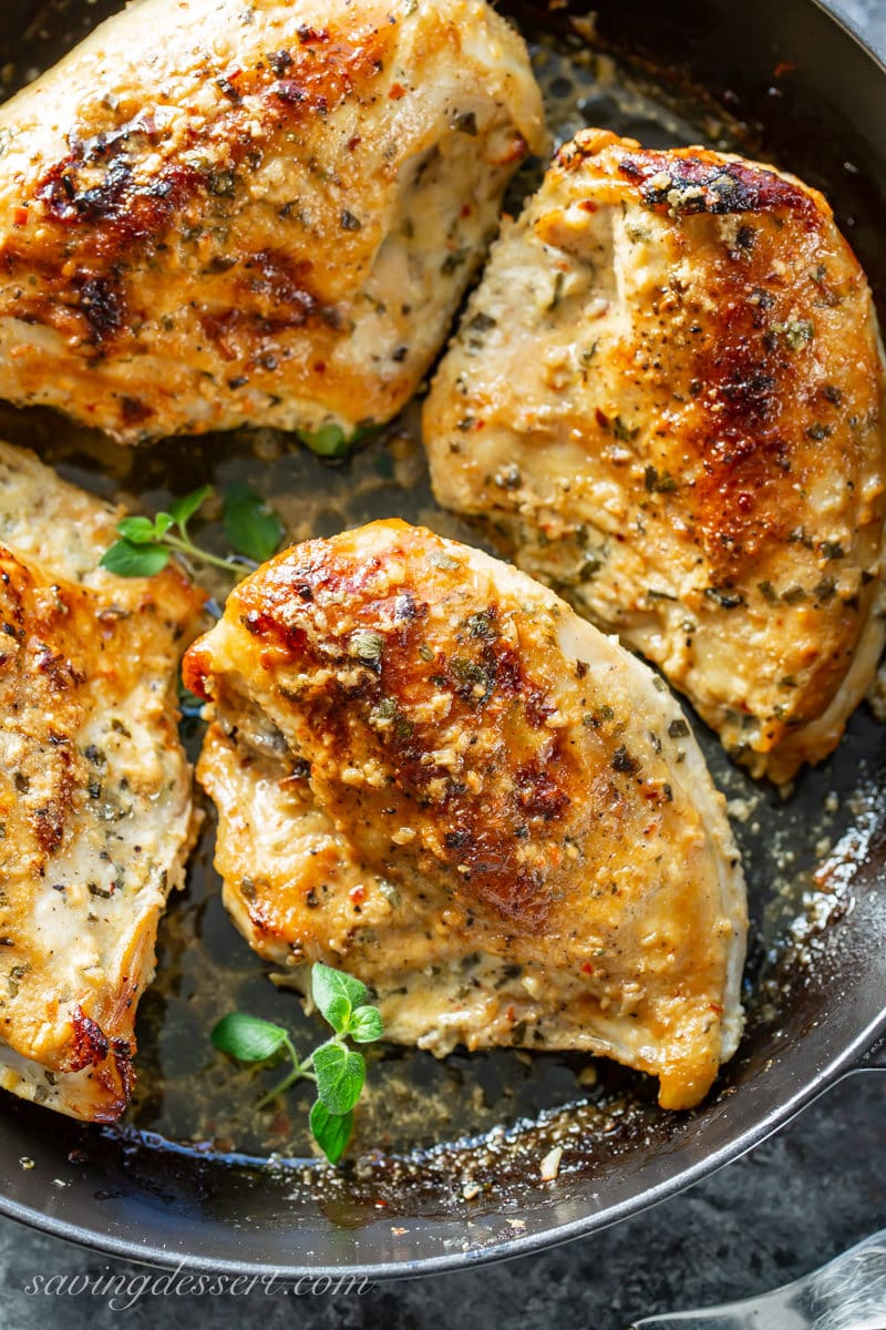 Juicy, plump, golden brown oven roasted chicken breasts in a pan with herbs and garlic.