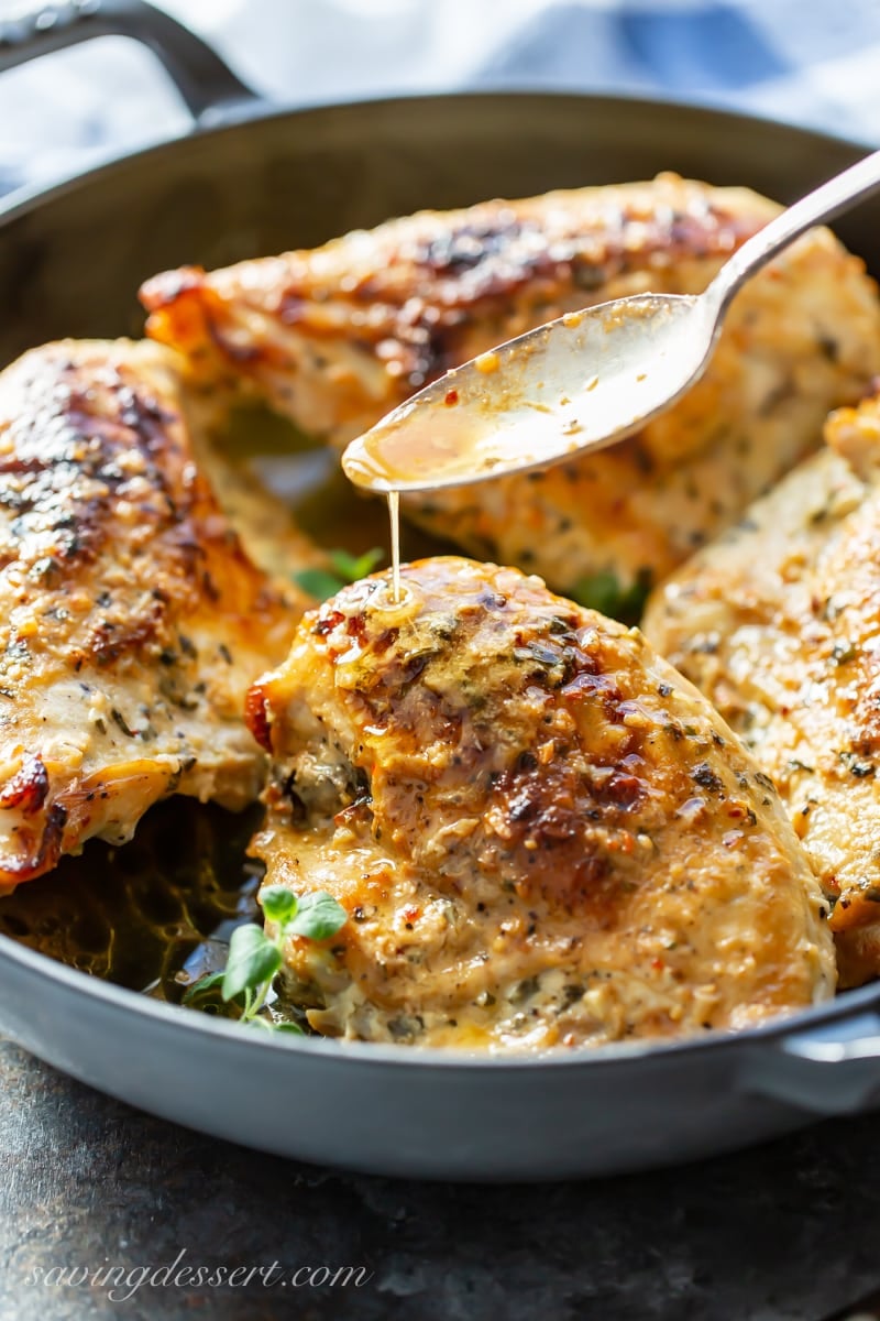 A skillet with bone-in, skin-on chicken breasts in a garlic, lemon butter sauce