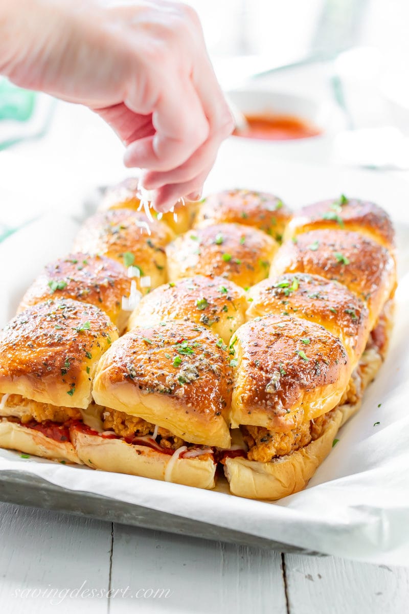 A tray of Chicken Parmesan Sliders topped with a garlic herb sauce and sprinkled with fresh parsley and grated Parmesan