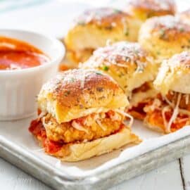 A platter filled with parmesan chicken sliders with a bowl of marinara on the side