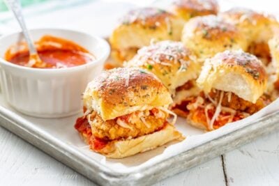 A platter filled with parmesan chicken sliders with a bowl of marinara on the side