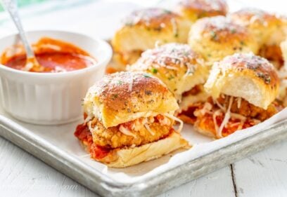A platter filled with parmesan chicken sliders with a bowl of marinara on the side