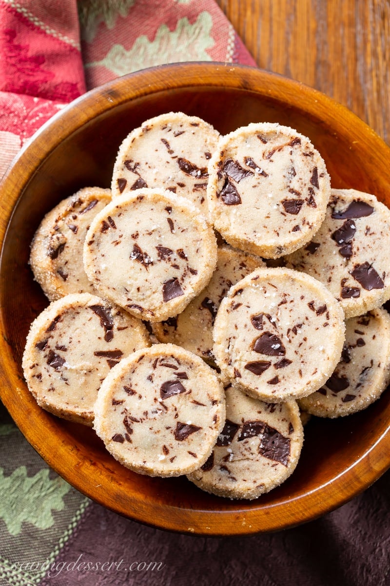 A wooden bowl filled with chocolate chunk shortbread cookies with sea salt