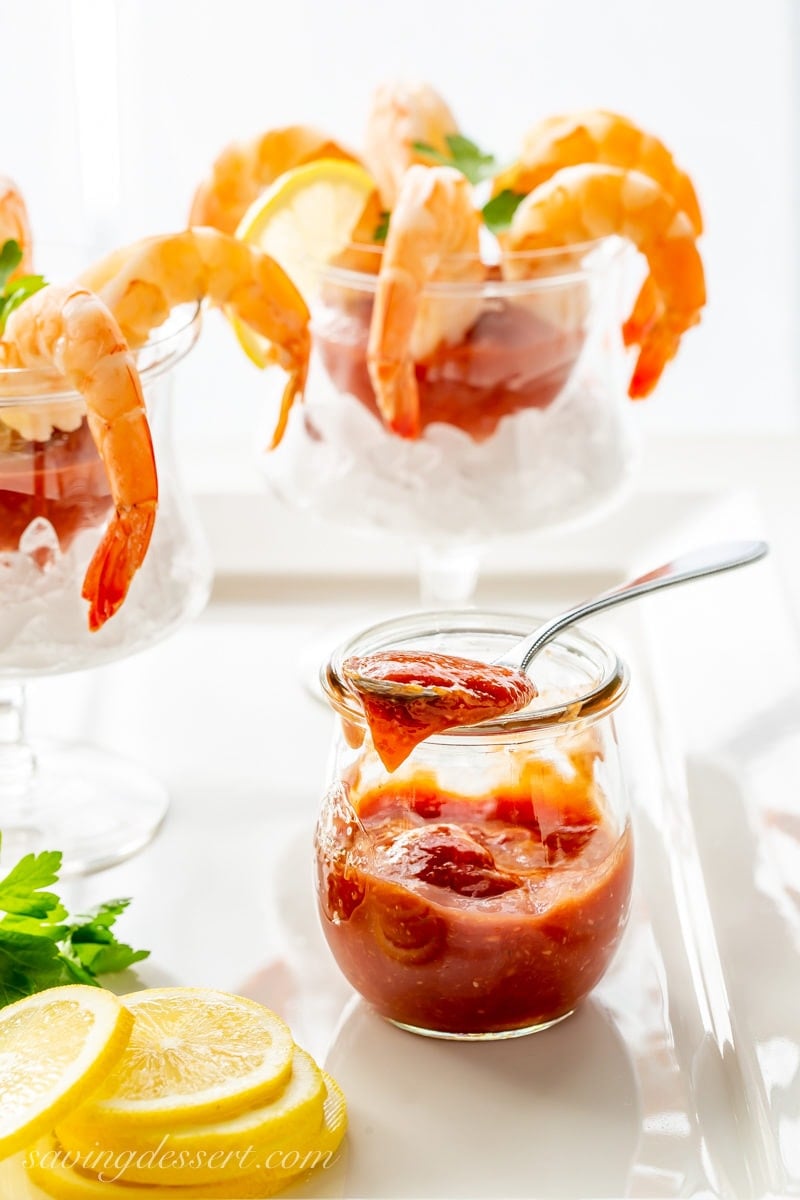 Glasses of shrimp with cocktail sauce, lemons and parsley and a jar of homemade cocktail sauce
