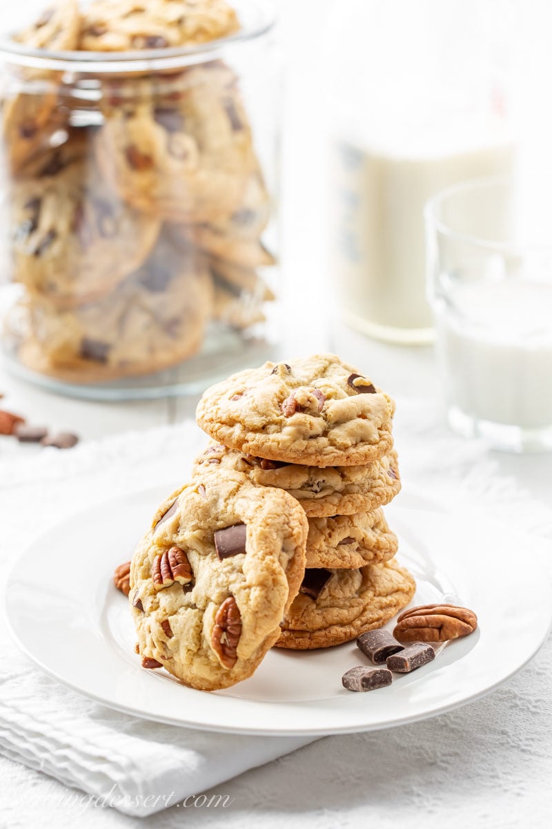 A stack of thick and chewy chocolate chunk cookies with pecans and a glass of milk