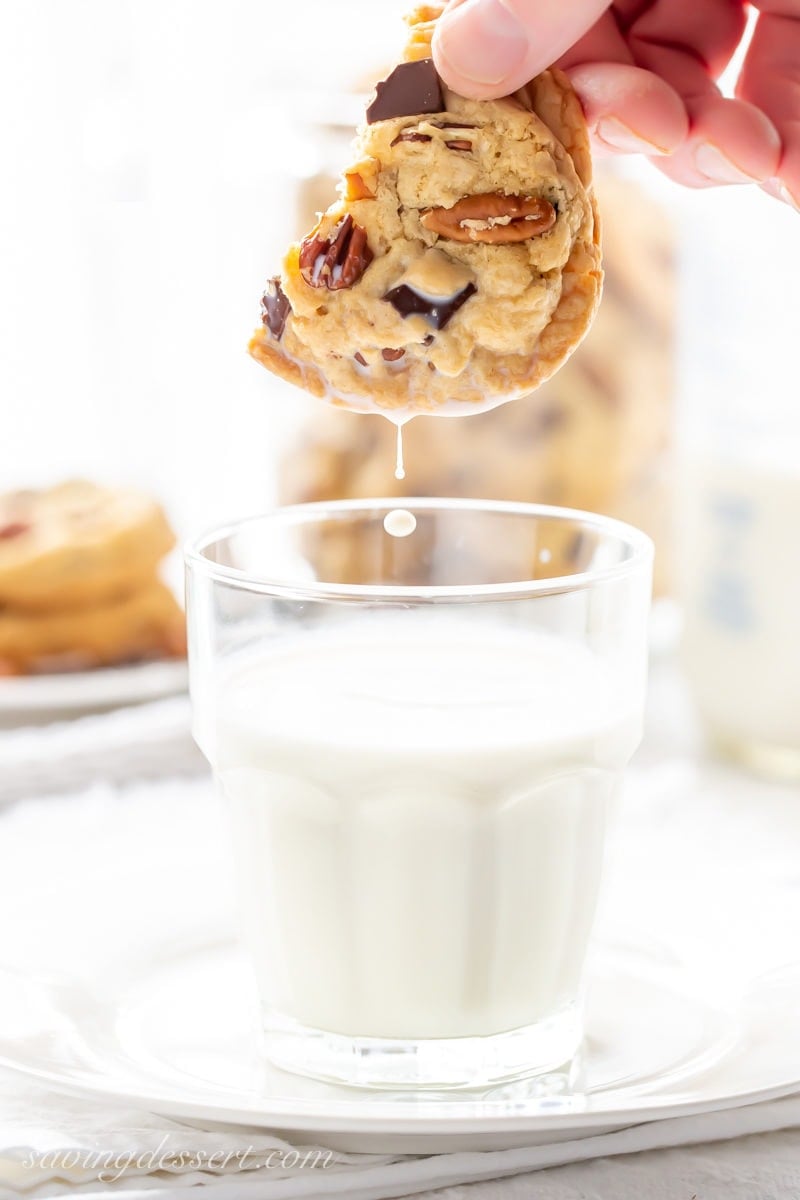 A large chocolate chunk cookie with pecans dunked in a glass of milk