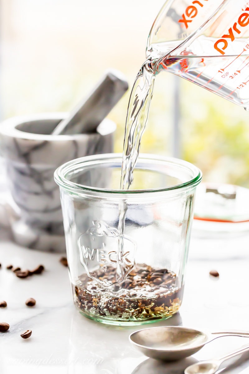 A jar with crushed coffee beans with vodka being poured into the jar