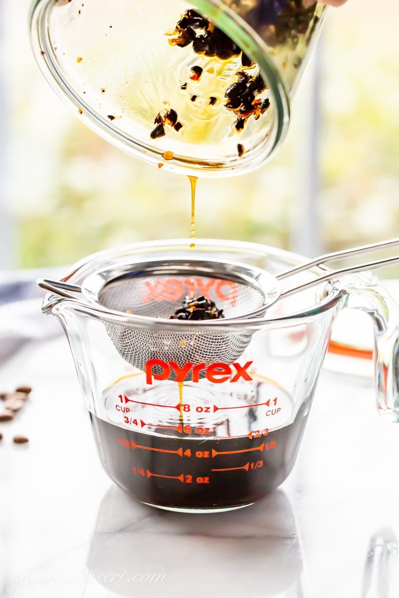 homemade coffee extract being poured through a fine mesh sieve to remove crushed coffee beans