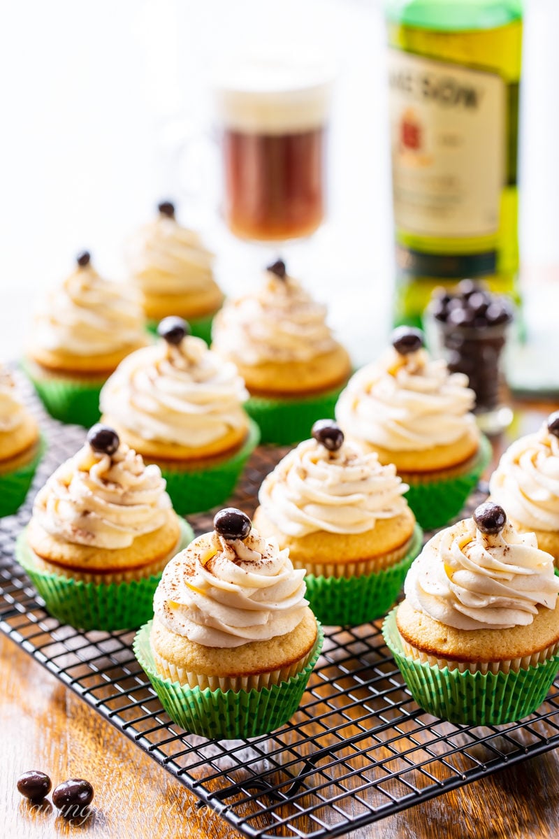 A cooling rack filled with Irish Coffee Cupcakes with swirled frosting topped with a chocolate covered espresso bean