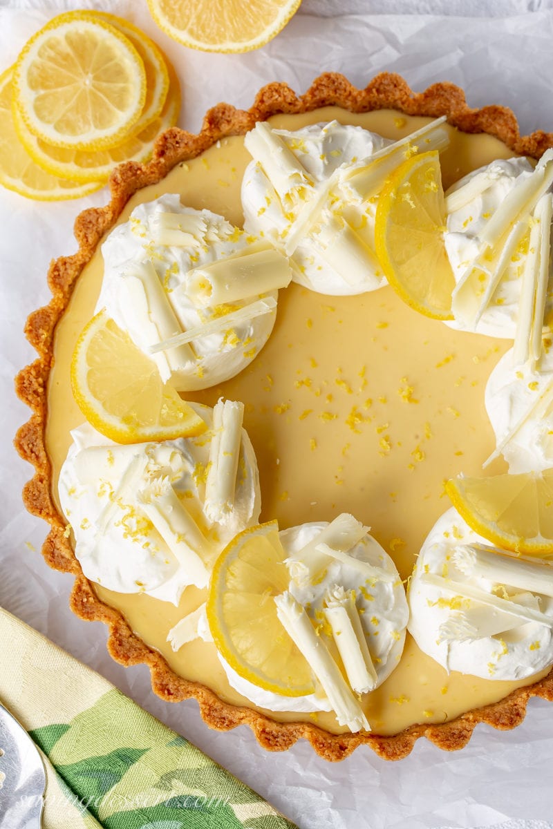 An overhead view of a lemon tart with mounds of whipped cream, lemon slices and chocolate curls.