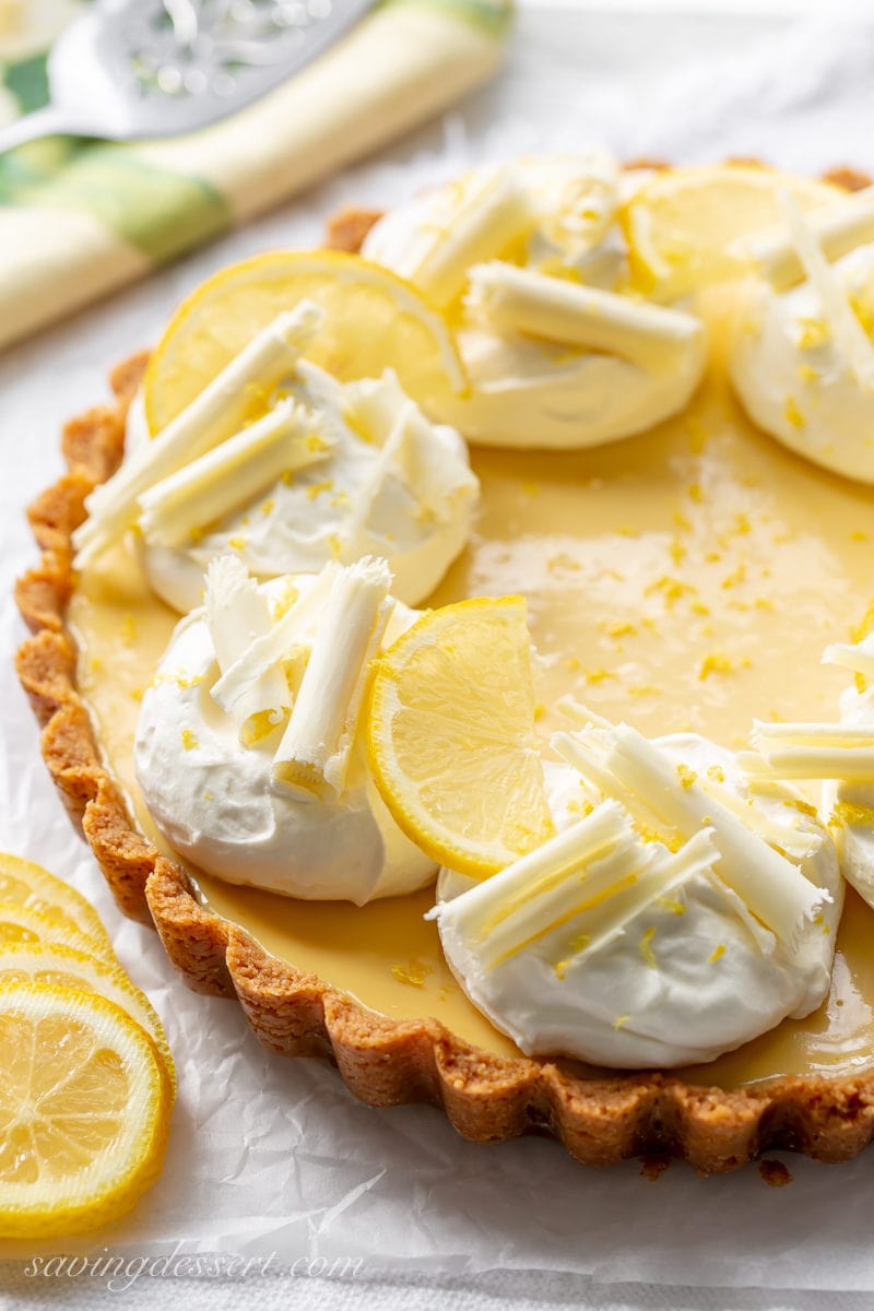 A lemon tart with graham cracker crust, mounds of whipped cream and chocolate curls