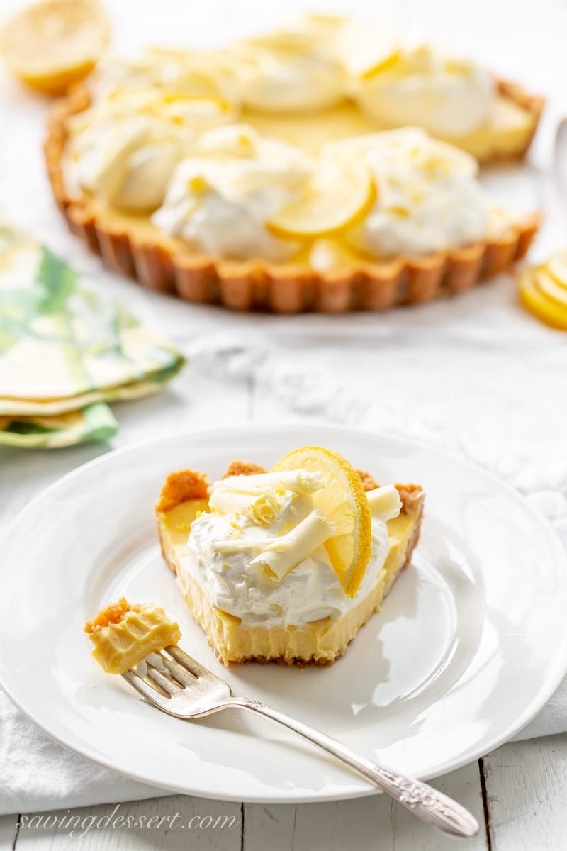 A slice of lemon pie topped with whipped cream, white chocolate curls and a slice of lemon