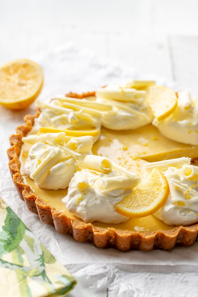 A creamy lemon tart with mounds of whipped cream, sliced lemons and white chocolate curls