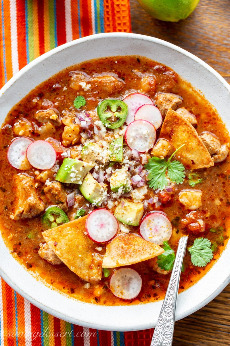 A bowl of Pork Posole topped with radishes, chips, avocado, cheese and cilantro