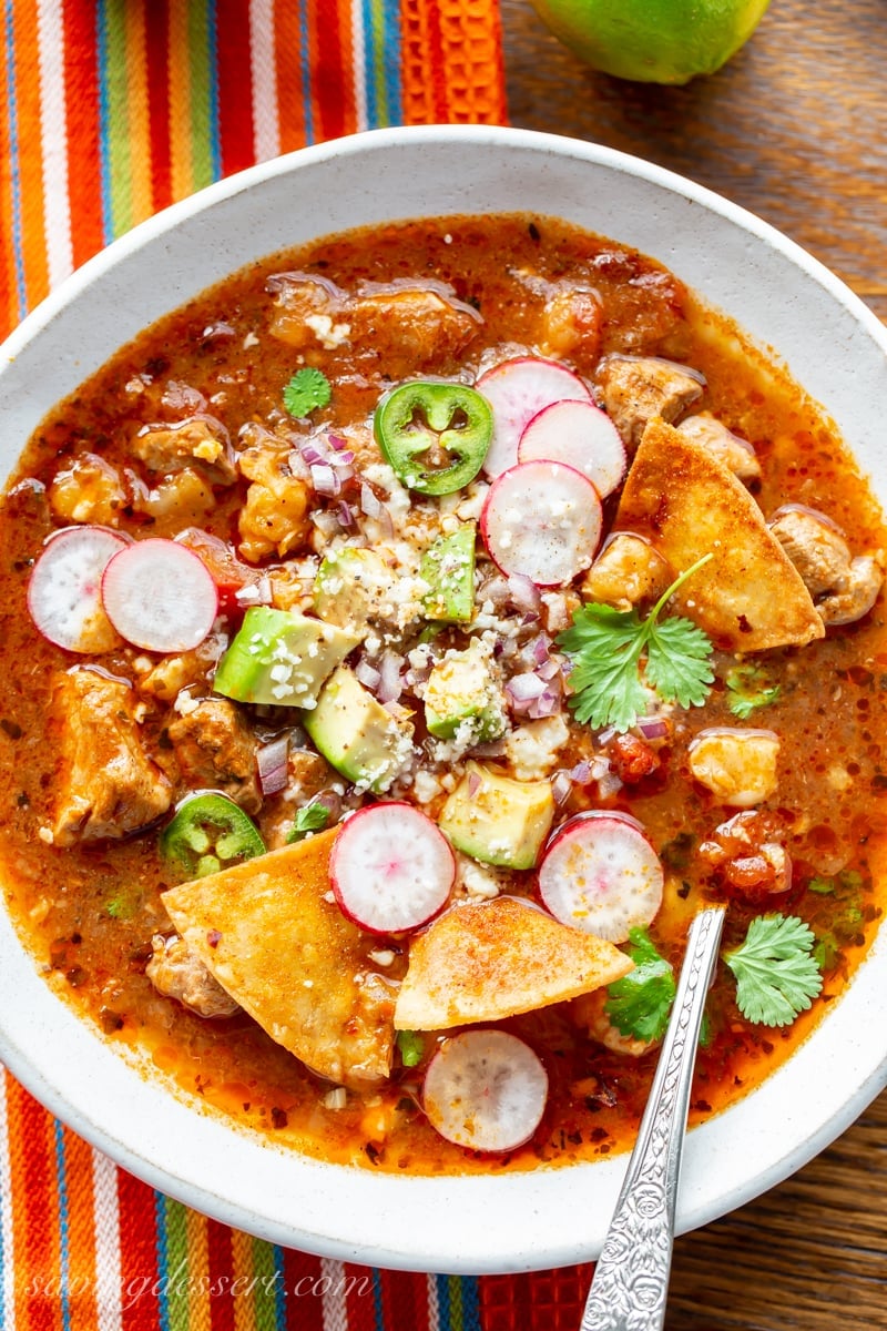 a bowl of pork posole topped with avocado, chips and cheese