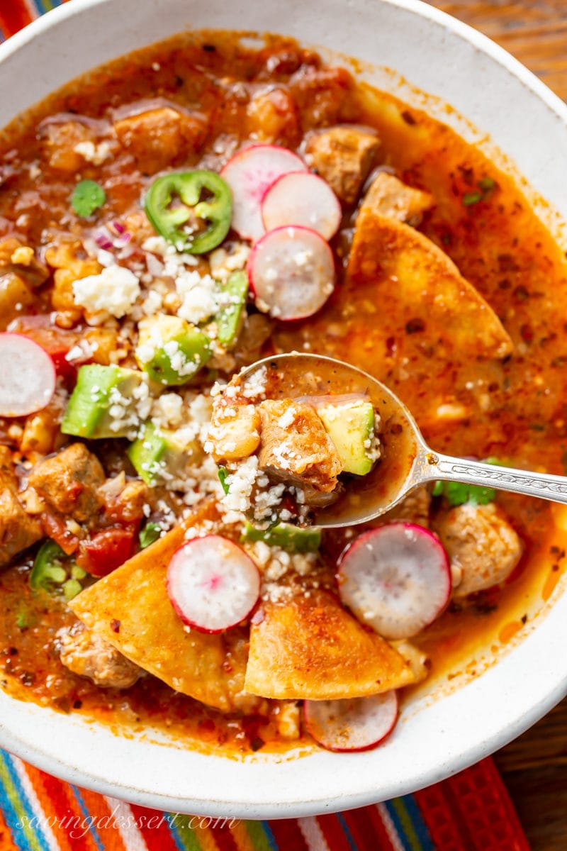 A bowl of pork posole with radishes, avocado, cotija cheese and chips